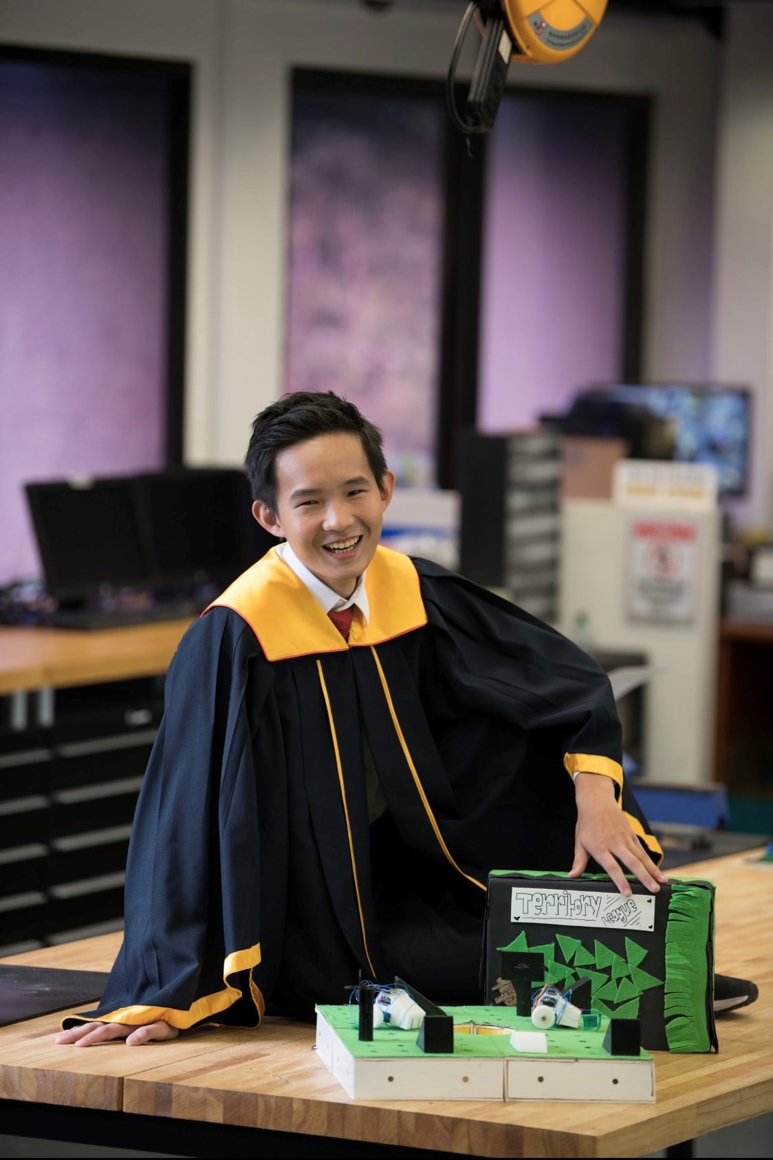 Lee Wen Wei in graduation attire at a Singapore Polytechnic workbench